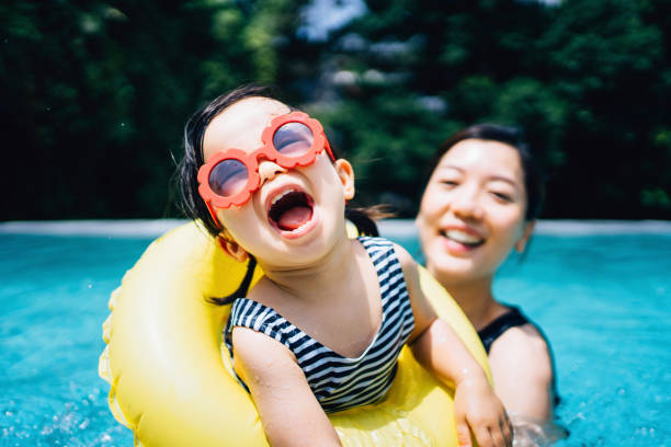 happy asian toddler girl with sunglasses smiling joyfully and enjoying family bonding time with mother having fun in the swimming pool in summer - travel stock-fotos und bilder