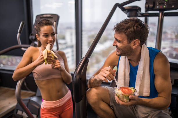 happy athletic couple eating healthy food on a break in a gym. - food stock pictures, royalty-free photos & images