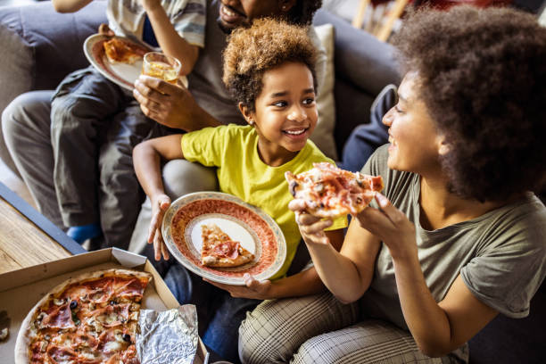 happy black mother and her daughter eating pizza at home. - junk food stock pictures, royalty-free photos & images