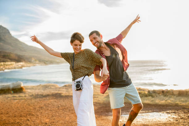 happy cheerful couple hand in hand at the coast at sunset - travel stock pictures, royalty-free photos & images
