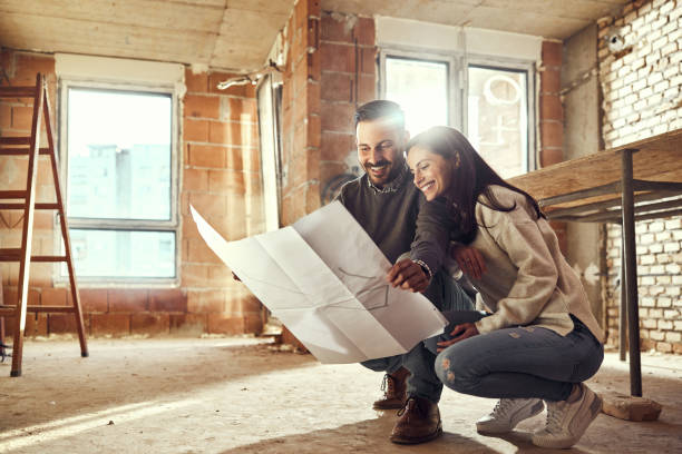 happy couple analyzing plans at their renovating apartment. - home decoration stock pictures, royalty-free photos & images