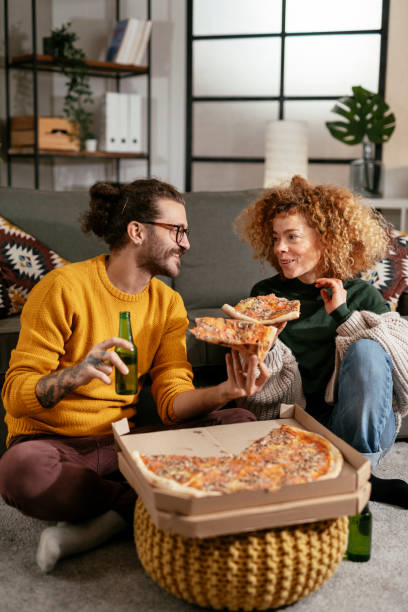 happy couple drinking beer and eating pizza, spending time together at home stock photo - junk food stock pictures, royalty-free photos & images
