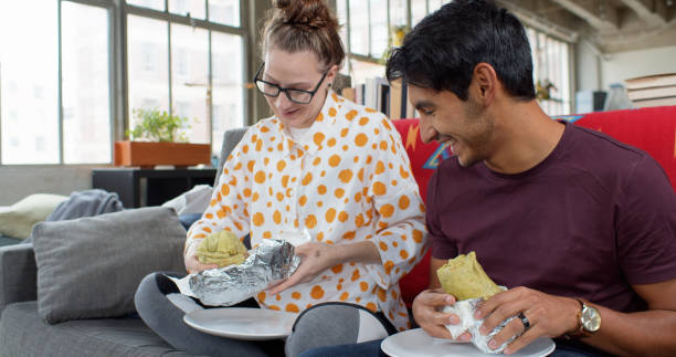 happy couple eating burritos at home - junk food stock pictures, royalty-free photos & images