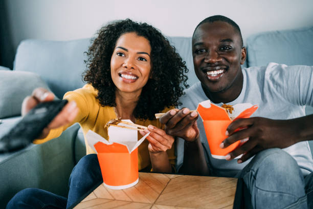 happy couple eating chinese food and watching tv at home. - junk food stock pictures, royalty-free photos & images
