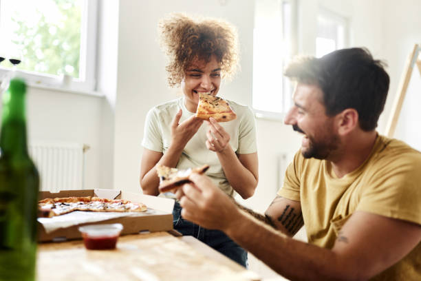 happy couple eating pizza at their new apartment. - junk food stock pictures, royalty-free photos & images