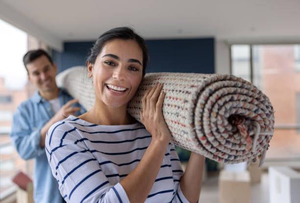 happy couple moving house and carrying a rolled up carpet - home decoration stock pictures, royalty-free photos & images