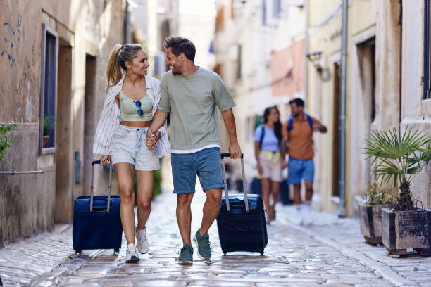 happy couple of tourists dragging their suitcases on the street. - travel stock pictures, royalty-free photos & images