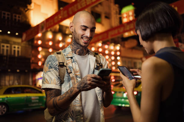 happy couple of tourists using smart phone on the city street at night. - fashion stock pictures, royalty-free photos & images