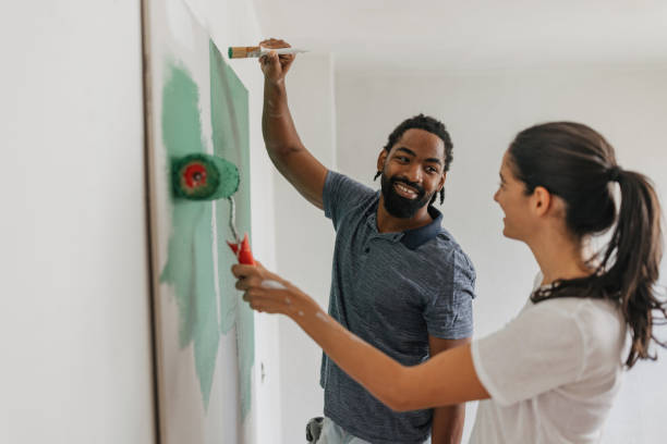 happy couple painting together with smiles - home decoration stock pictures, royalty-free photos & images