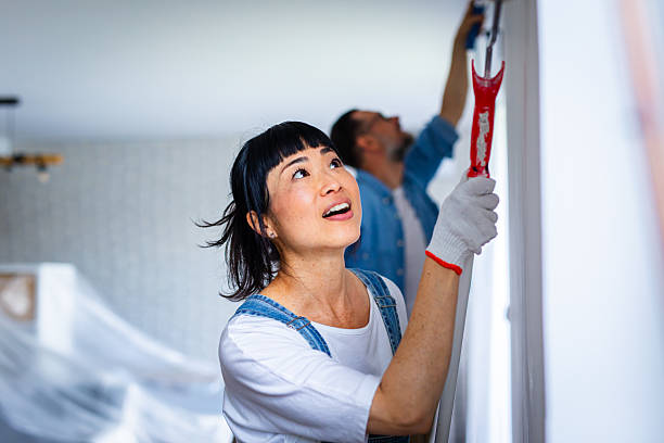 happy couple renovating their home, painting the wall and smiling while working together - home decoration stock pictures, royalty-free photos & images