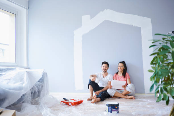 happy couple taking break from painting walls in new apartment - home decoration fotografías e imágenes de stock