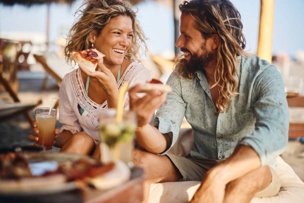 happy couple talking while eating pizza in a beach bar. - home decoration stock pictures, royalty-free photos & images