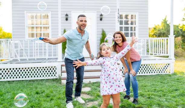 happy family playing soap bubbles on the grass in front of their porch. adorable little girl playing soap bubbles with her mother and father outdoors. - garden decoration stock pictures, royalty-free photos & images
