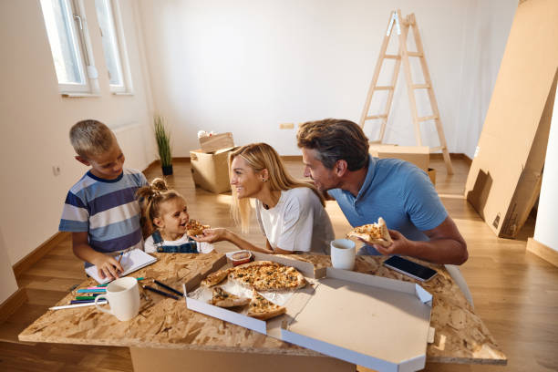 happy family talking while eating pizza after unpacking their belongings in new home. - junk food stock pictures, royalty-free photos & images