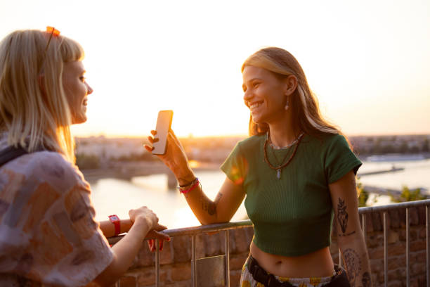 happy female friends using mobile phone at sunset. - concert stock pictures, royalty-free photos & images