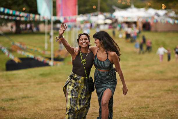 happy female friends walking with arms around at park - concert stock pictures, royalty-free photos & images