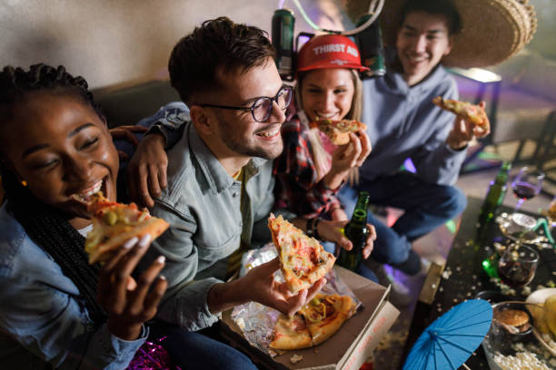 happy friends eating pizza for dinner on a party at home. - junk food stock pictures, royalty-free photos & images