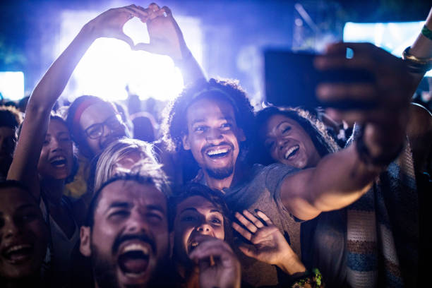 happy friends taking a selfie on music festival by night. - concert stock pictures, royalty-free photos & images
