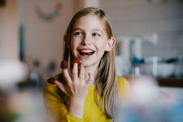happy girl sitting at kitchen table at home playing with raspberries - food stock pictures, royalty-free photos & images