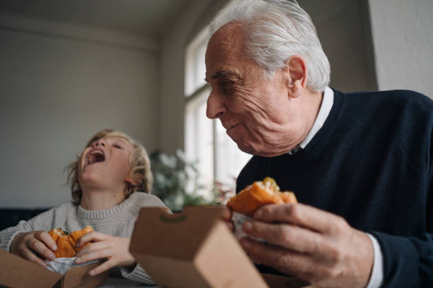 happy grandfather and grandson eating burger together at home - junk food stock pictures, royalty-free photos & images
