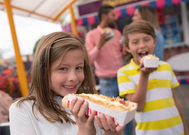 happy kids eten junkfood bij een pretpark - junk food stockfoto's en -beelden