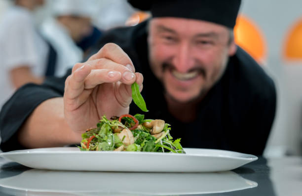happy male chef adding details to a salad and smiling - home decoration stock pictures, royalty-free photos & images