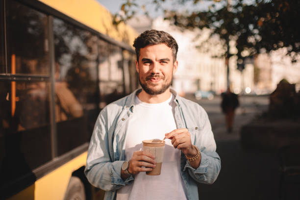 happy man holding cup of coffee while standing on street during summer - junk food stock pictures, royalty-free photos & images