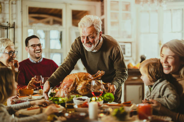 happy senior man serving thanksgiving turkey for his family at dining table. - home decoration stock pictures, royalty-free photos & images