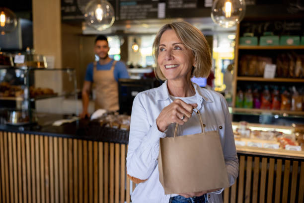 happy woman leaving a cafe carrying a bag of pastries - junk food stock pictures, royalty-free photos & images