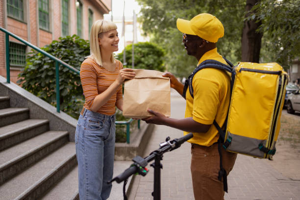 happy woman receiving her order from black delivery guy. - junk food stock pictures, royalty-free photos & images