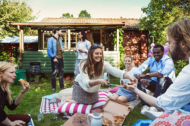 happy woman serving pizza to friends in backyard during summer party - junk food stock pictures, royalty-free photos & images