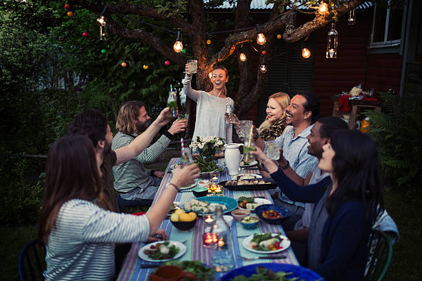 happy woman toasting drink to friends at dining table while enjoying outdoor dinner party - garden decoration stock pictures, royalty-free photos & images