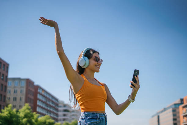 happy woman wearing headphones and using phone in the city - fashion stock pictures, royalty-free photos & images