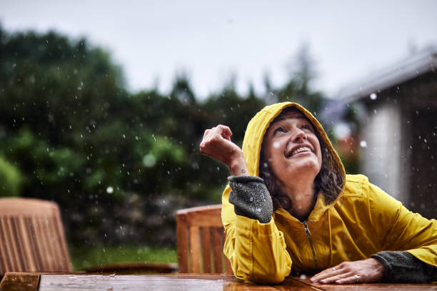 happy woman wearing raincoat during heavy rain in garden - garden decoration photos et images de collection