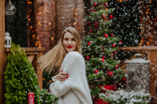 happy woman with blond hair standing under the snowfall in front yard - garden decoration stock pictures, royalty-free photos & images