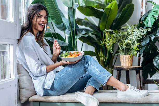 happy woman with bowl of salad at the window - food photos et images de collection