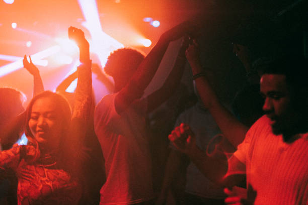 happy young male and female friends enjoying dance at illuminated red nightclub - concert stock pictures, royalty-free photos & images