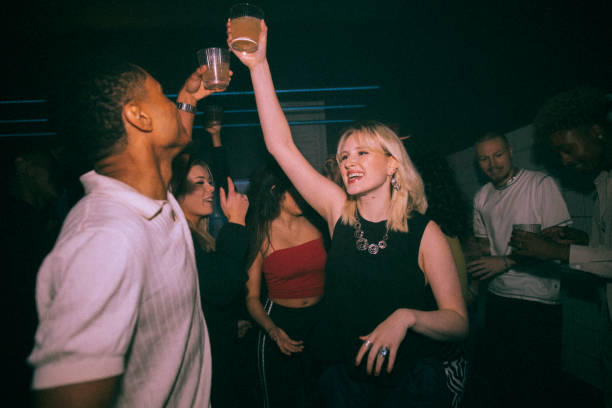 happy young woman and man toasting drinks while dancing against friends at nightclub - concert stock pictures, royalty-free photos & images