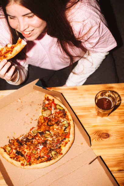happy young woman eating pizza at house party - junk food stock pictures, royalty-free photos & images