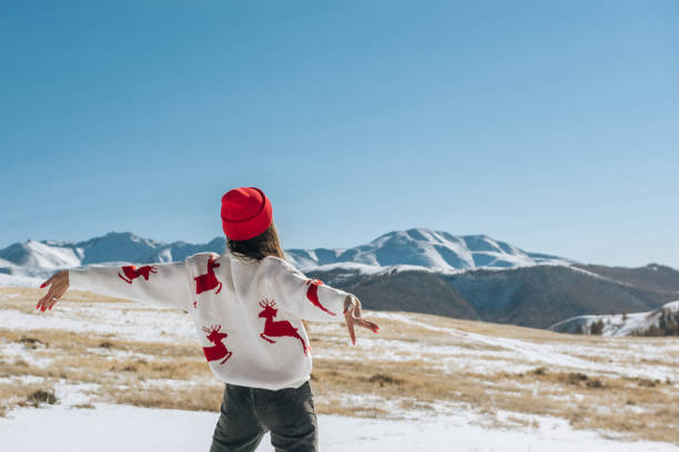 happy young woman with raised hands on the background of blue sky and winter mountains in winter looking at the landscape. christmas travel concept - travel photos et images de collection