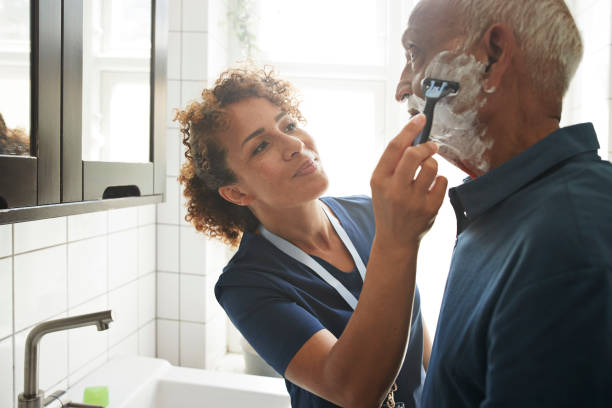 healthcare worker assisting senior man in shaving - hairstyle stock pictures, royalty-free photos & images
