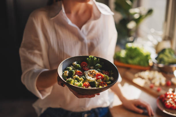 healthy dinner or lunch. woman in t-shirt and jeans standing and holding vegan superbowl or buddha bowl with hummus, vegetable, salad, beans, couscous and avocado and smoothie in hands, square crop - food stock pictures, roya