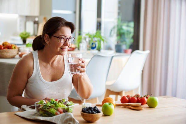healthy eating concept. woman drinkig water while having a healthy meal of salad and fruits - food stock pictures, royalty-free photos & images