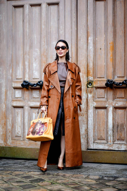 Heart Evangelista wears a brown leather trench long coat , a dark brown leather top, a bb leather midi slit skirt , a large brown leather Hermes...