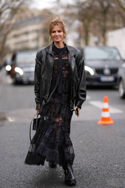 Helena Bordon wears silver earrings, a black leather oversized jacket, a black long lace dress, a black leather bag, black leather shoes, outside...