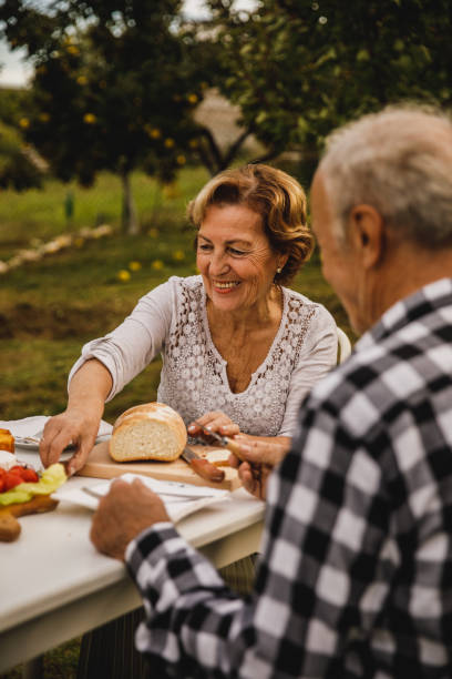 heureux couple de personnes âgées assis à table dans leur cour arrière, se liant et soupant - garden decoration photos et images de collection