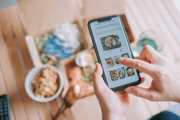 high angle view close up asian woman using meal delivery service ordering food online with mobile app on smartphone in the living room at a cozy home - food stock pictures, royalty-free photos & images