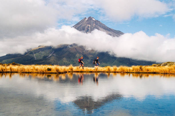 hikers reflection of mount taranaki egmont in natural lake middle - travel stock pictures, royalty-free photos & images
