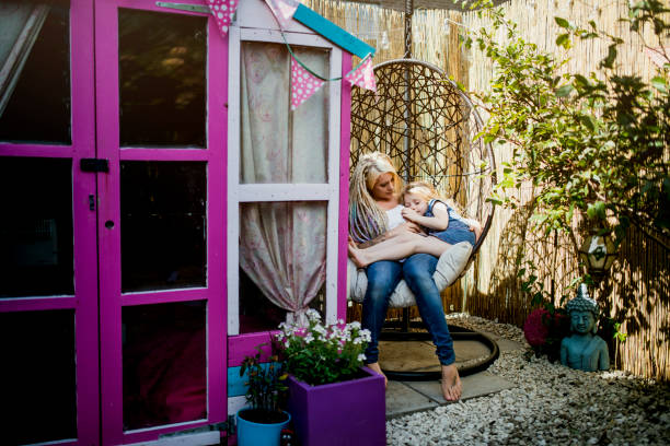 hipster mother sitting in the back yard swing with daughter - garden decoration stock pictures, royalty-free photos & images