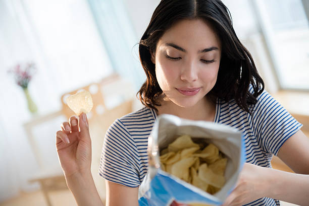 hispanic woman reading ingredients on bag of potato chips - junk food stock pictures, royalty-free photos & images